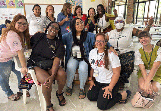 Image slideshow: Group photo of participants inside a classroom, one person hands seeds to another, group shot of the U.S. delegation, participants taking notes outside, visiting Berta's grave, visiting COPINH, the week's agenda